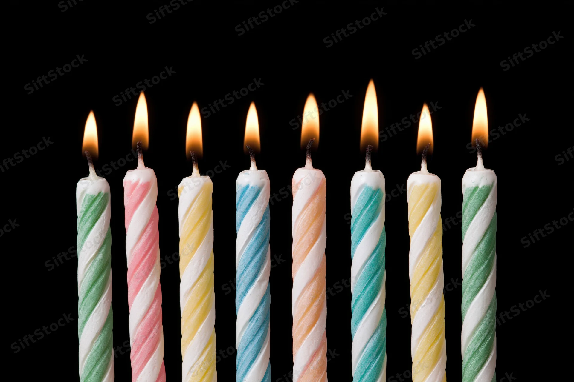 Eight lit birthday candles in a row against a black background