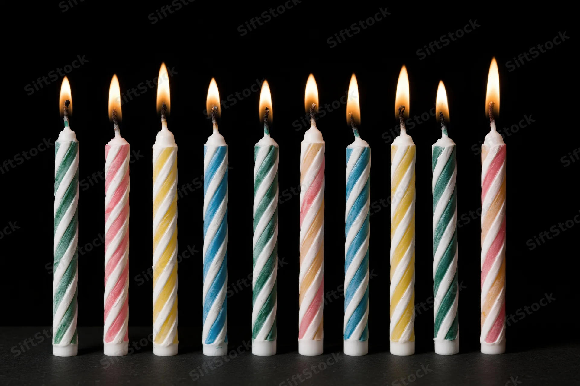 Eight lit birthday candles in a row against a black background