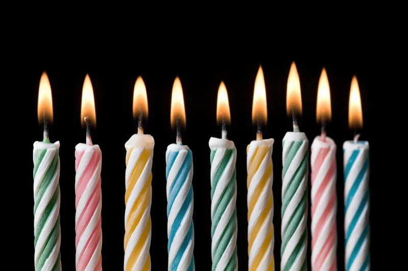 Eight lit birthday candles in a row against a black background