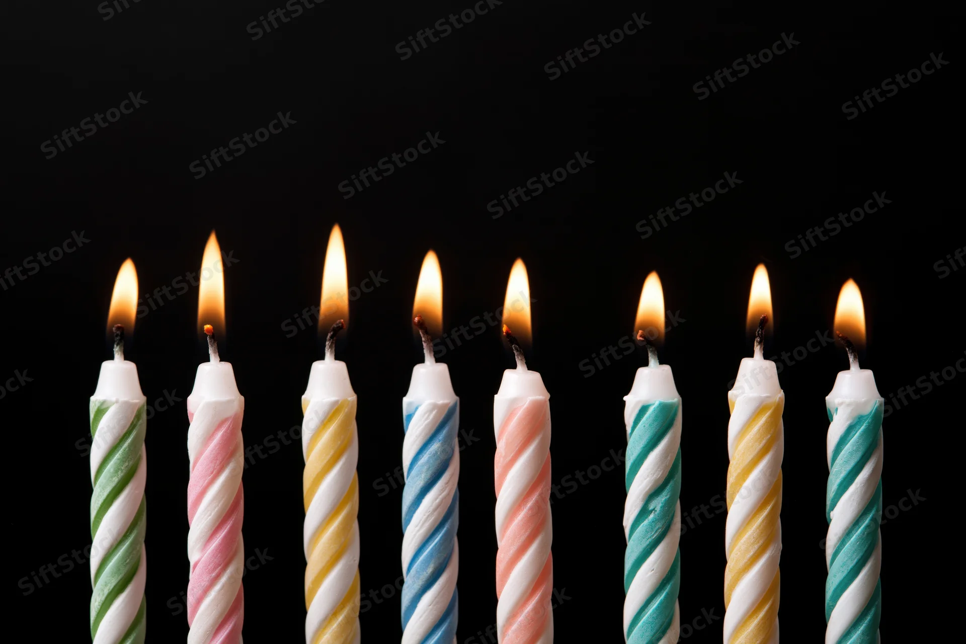 Eight lit birthday candles in a row against a black background with copyspace