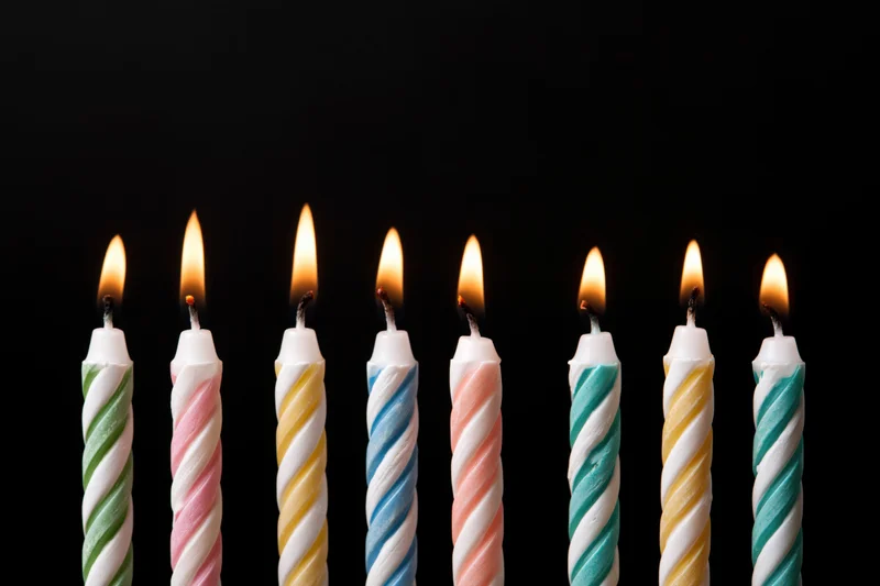 Eight lit birthday candles in a row against a black background with copyspace