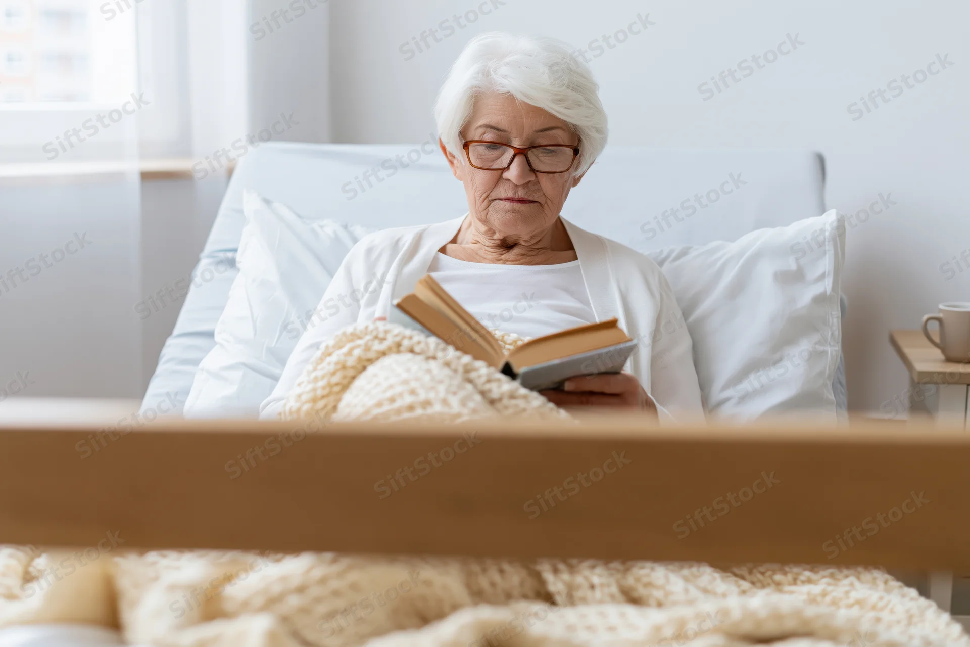 Elderly woman reading a book in bed at home