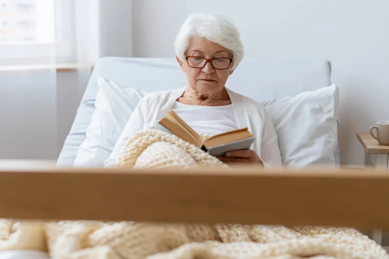 Elderly woman reading a book in bed at home
