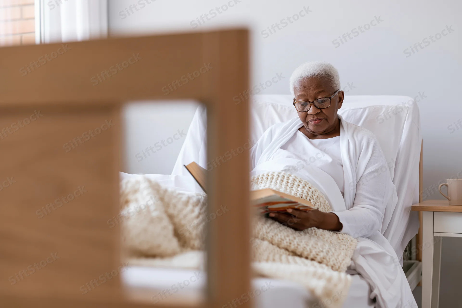 Senior woman reading a book in bed at a nursing home