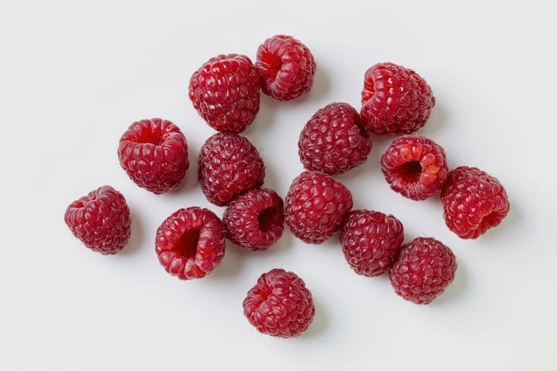 Fresh raspberries scattered on a white surface