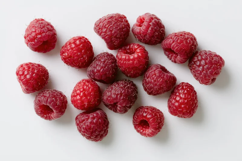 Fresh raspberries scattered on a white surface in a studio overhead view