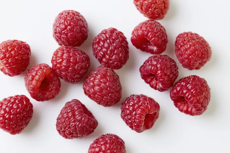 Fresh raspberries scattered on a white surface