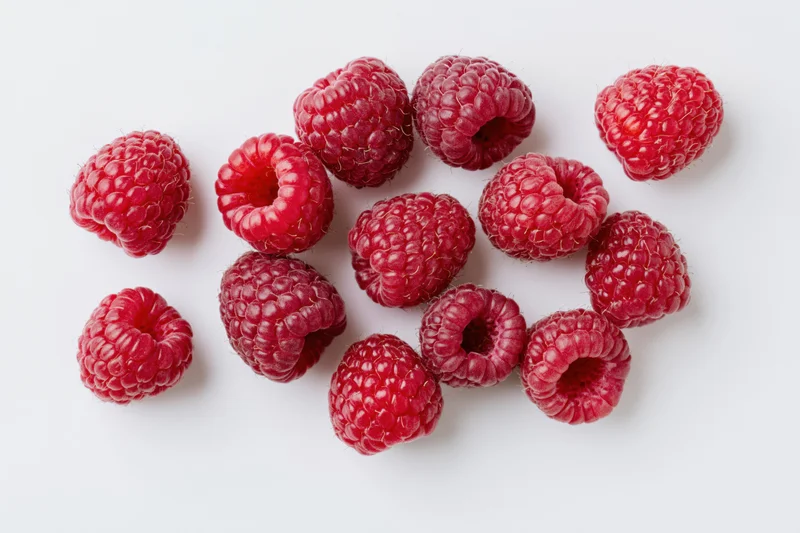Fresh raspberries scattered on a white surface