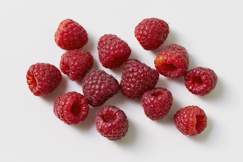 Fresh raspberries scattered on a white surface
