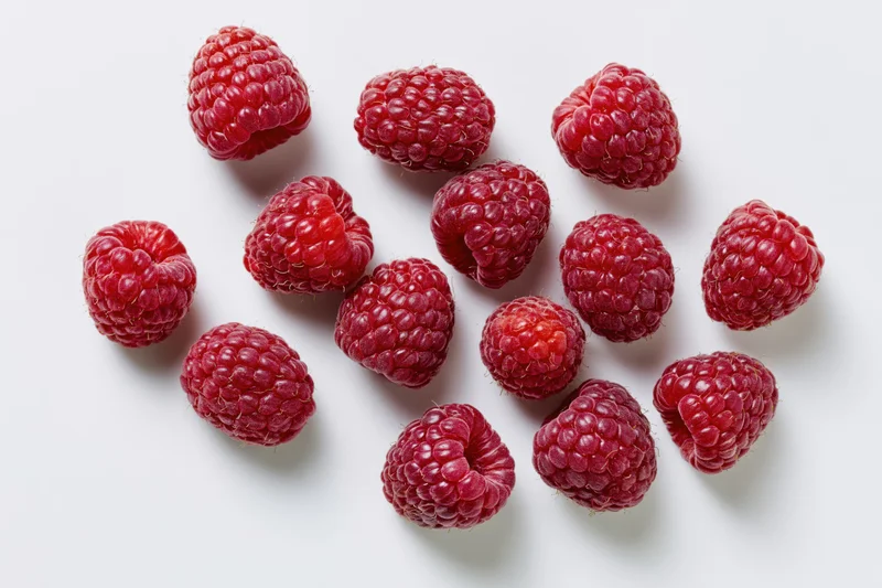 Fresh raspberries scattered on a white surface