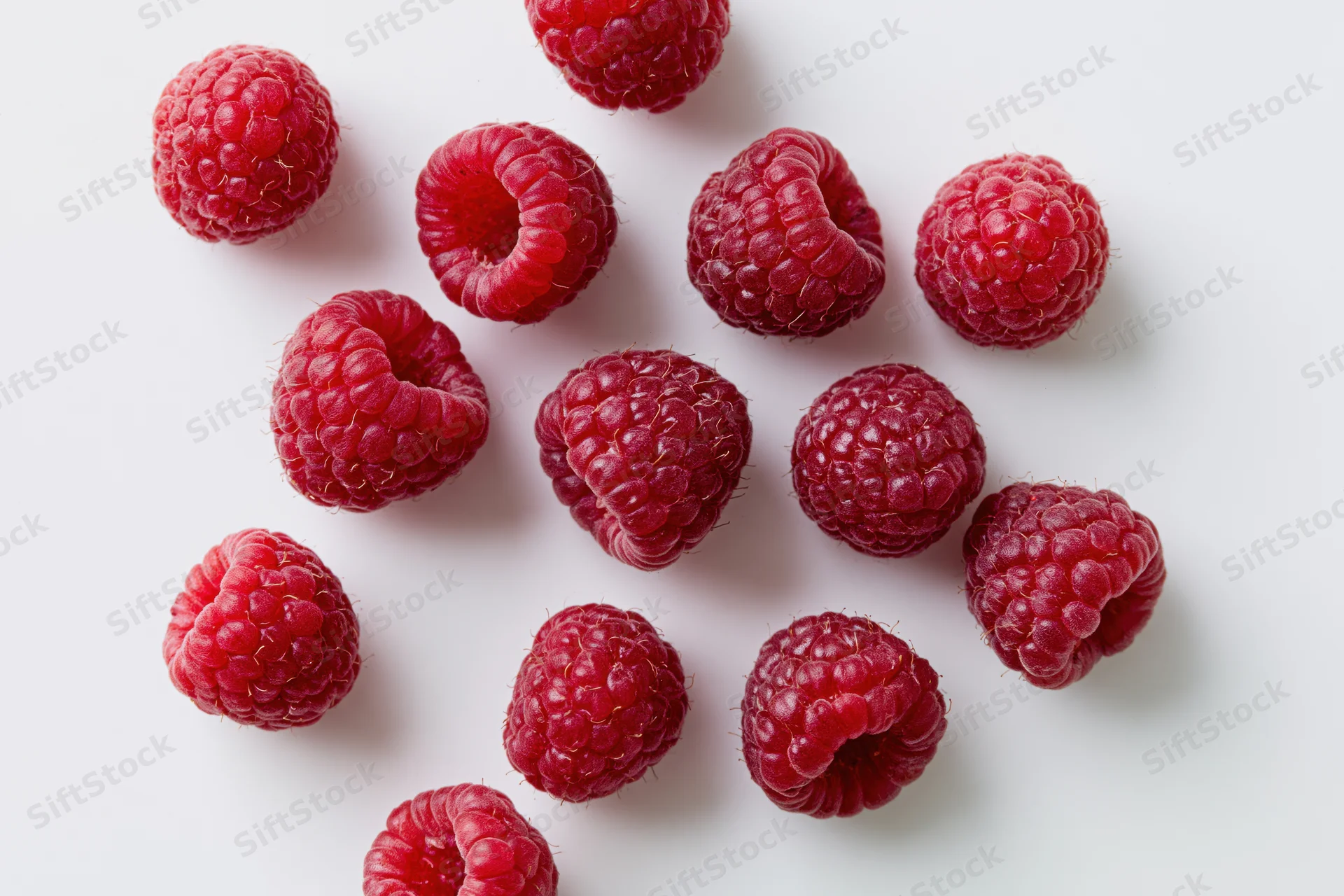 Fresh raspberries scattered on a white surface in a flat lay view