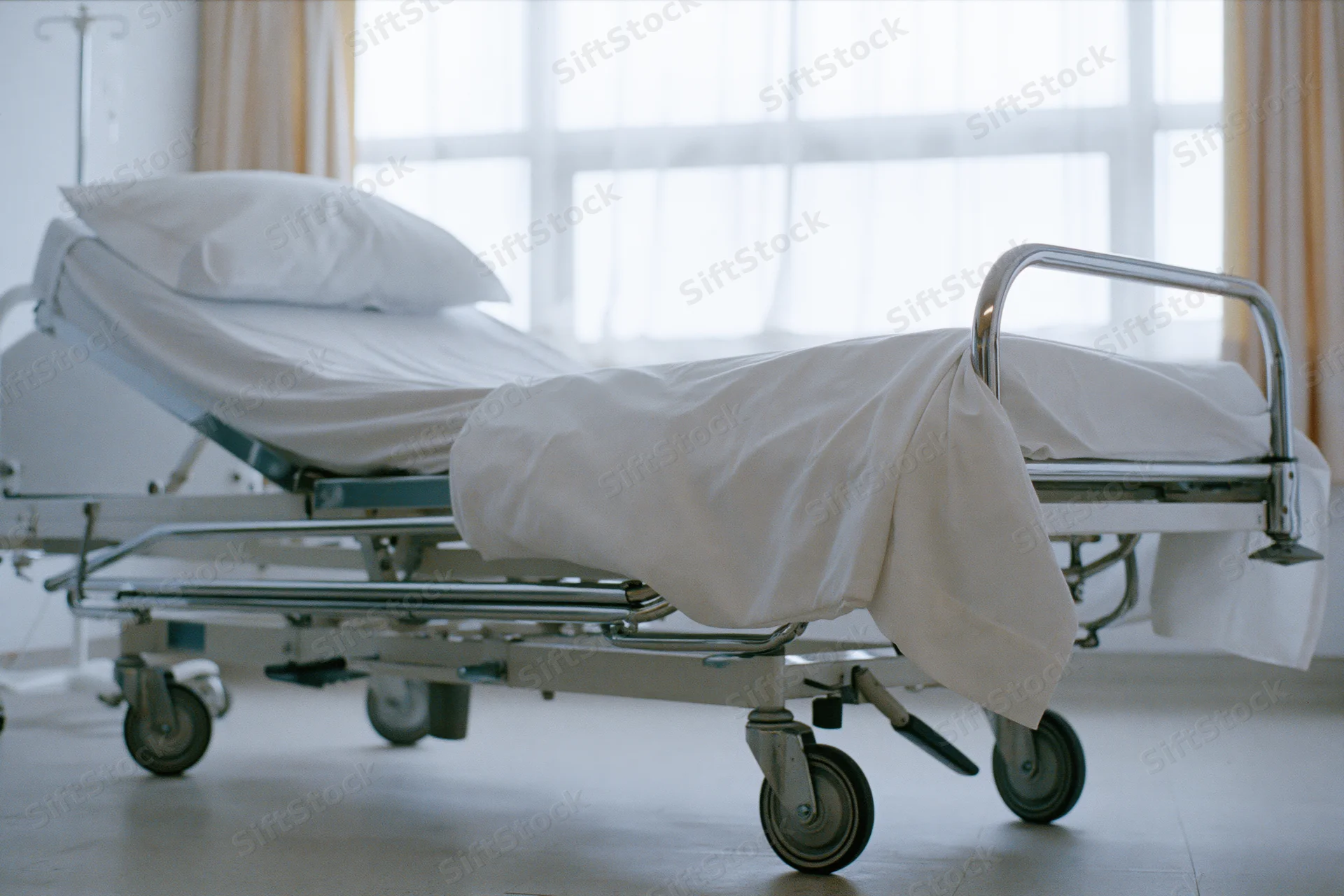 Empty adjustable hospital bed with white linens and chrome frame in a clinical room