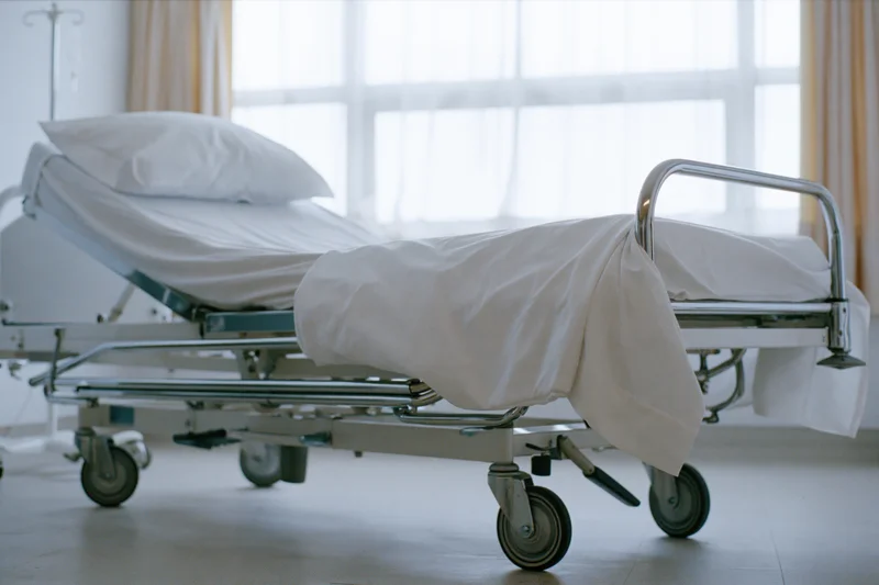 Empty adjustable hospital bed with white linens and chrome frame in a clinical room