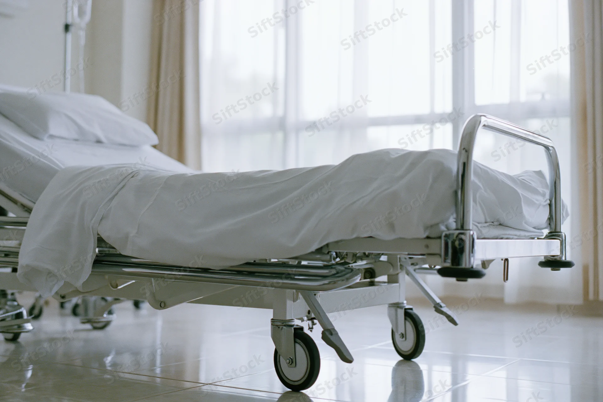 Empty adjustable hospital bed with white linens and chrome frame in a clinical room