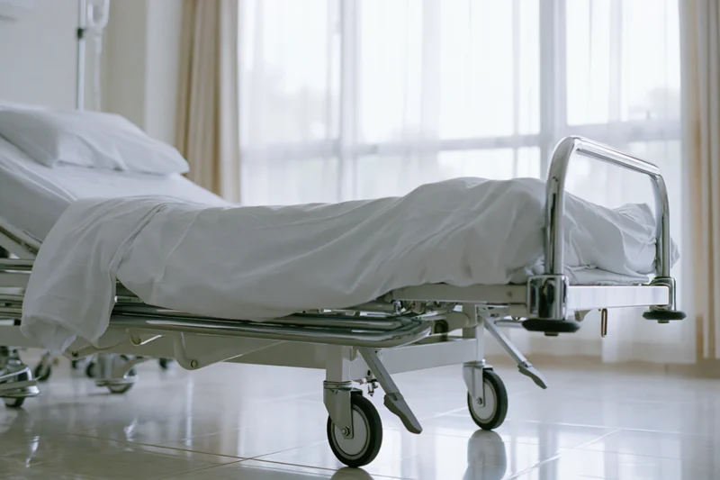 Empty adjustable hospital bed with white linens and chrome frame in a clinical room