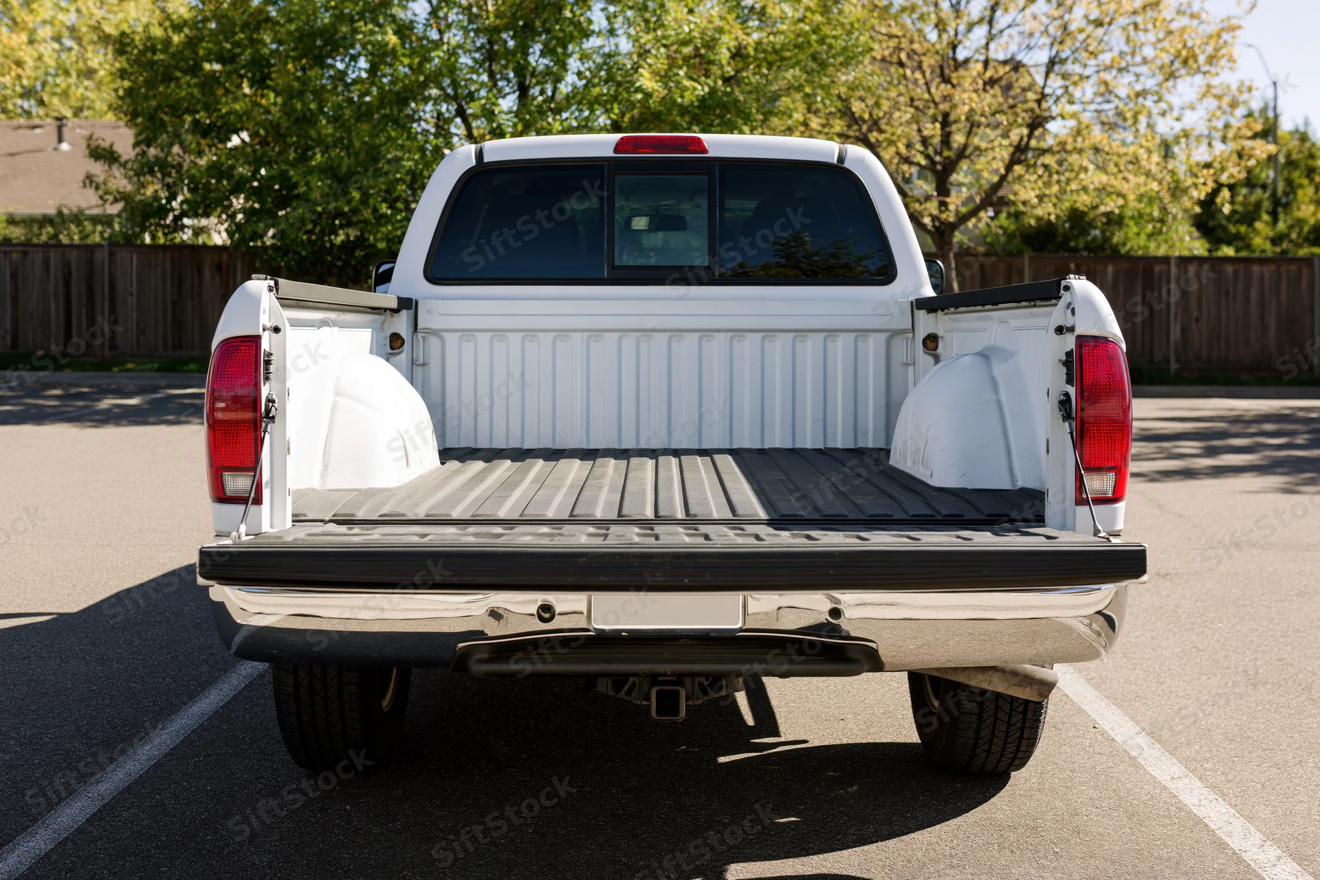 Rear view of a white pickup truck with empty bed parked in a suburban driveway