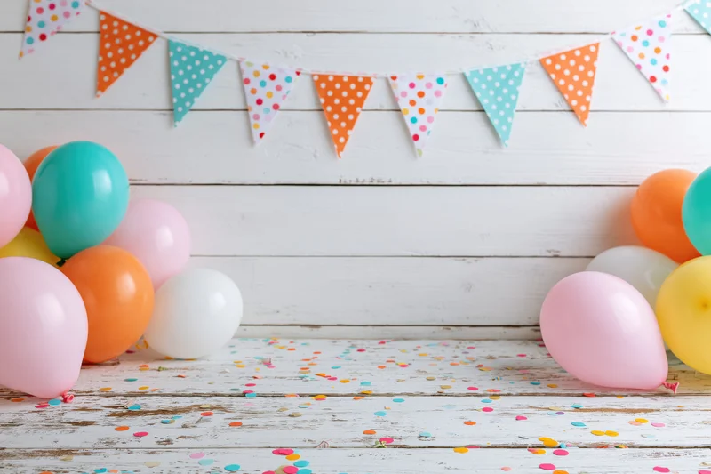 Colorful balloons and polka-dot banner arranged on white wooden floor with scattered confetti for birthday party setup