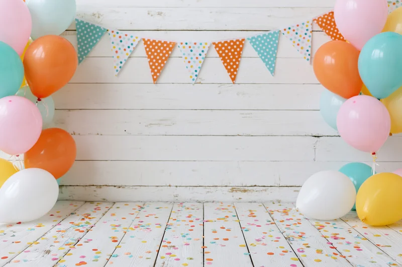 Colorful balloons and confetti on white wooden floor with banner against rustic wall