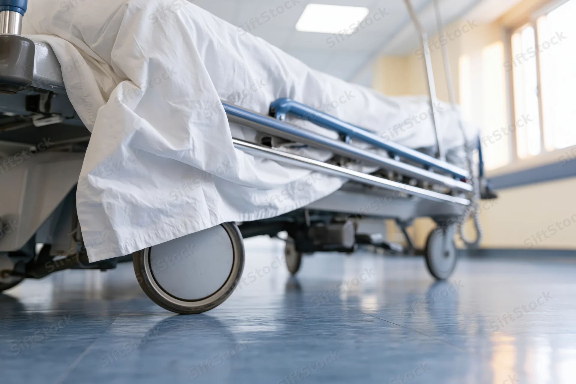 Hospital gurney with white rumpled sheets on metal frame in corridor