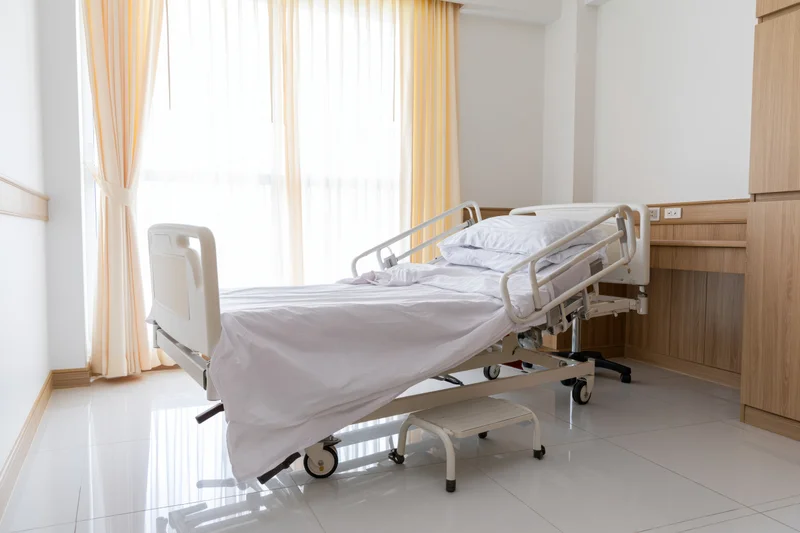 Adjustable medical bed in a private hospital room with window and wooden furniture