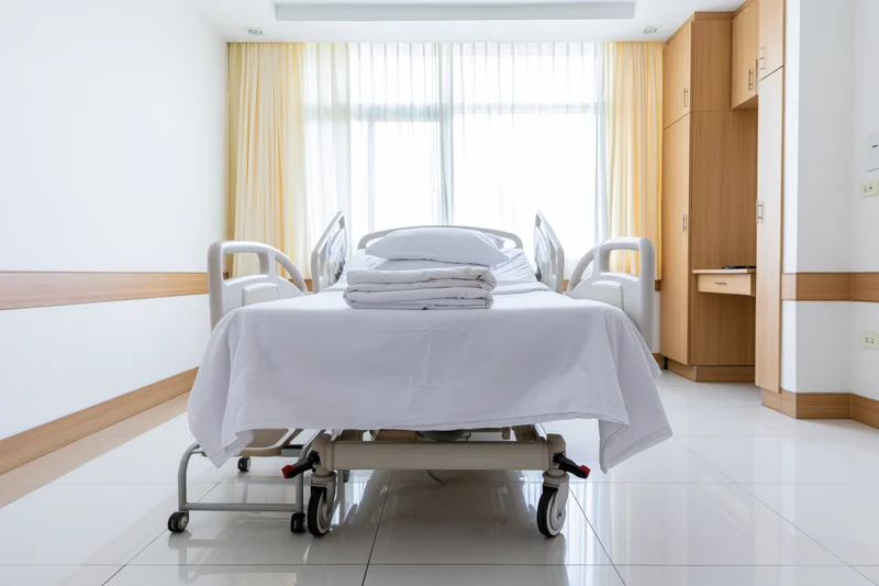 Adjustable medical bed in a clean private hospital room with white linens and wooden cabinetry