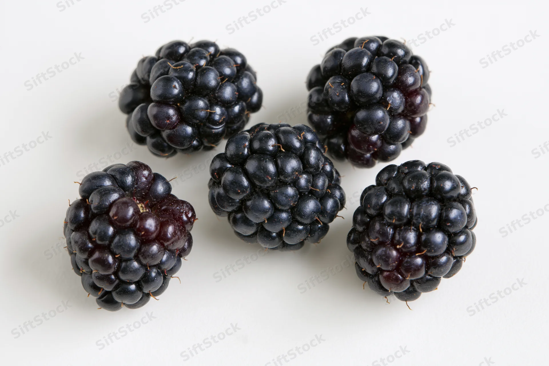 Five ripe blackberries scattered on a white surface
