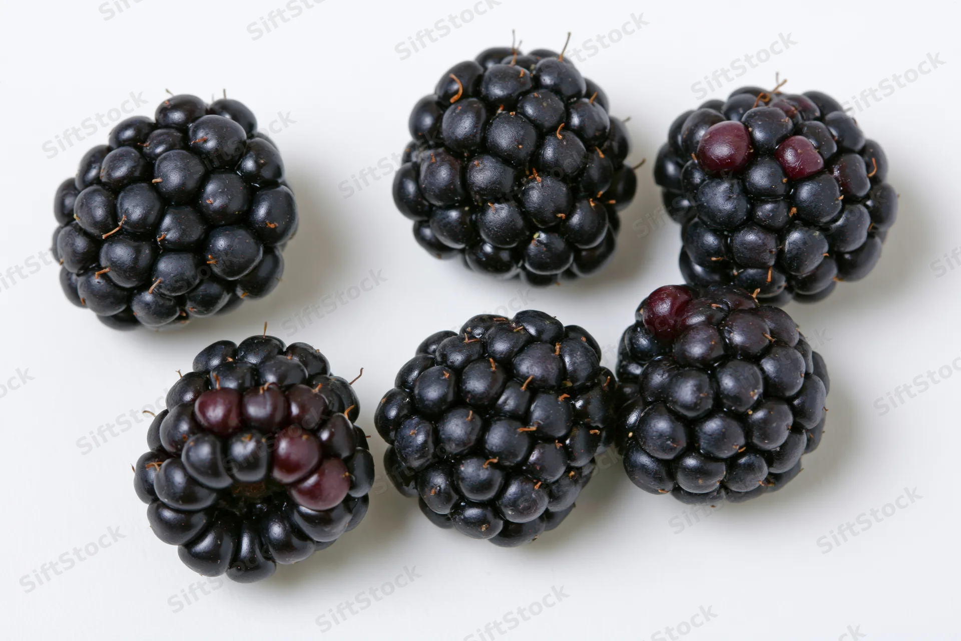 Five ripe blackberries scattered on a white surface