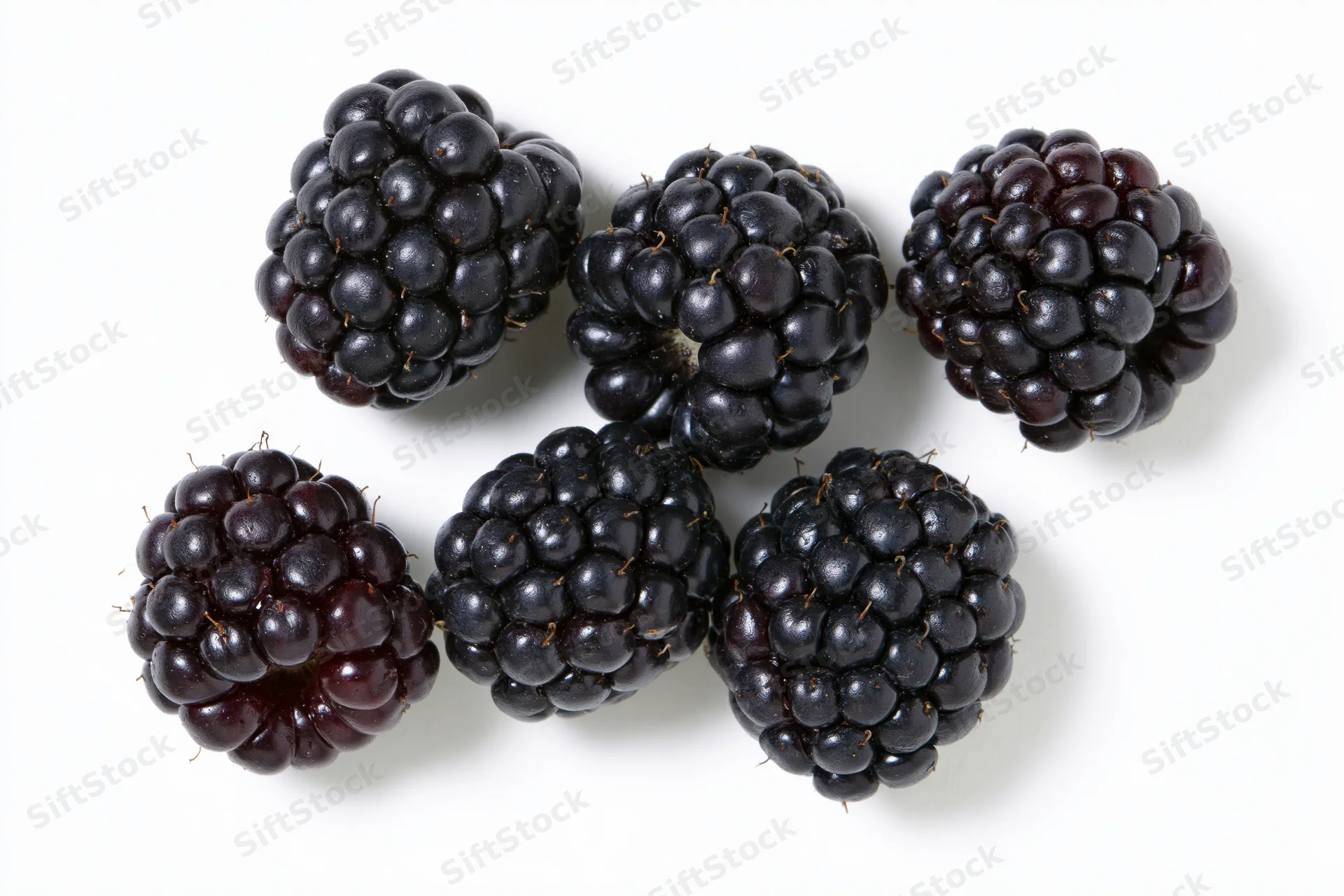 Six ripe blackberries scattered on a white surface