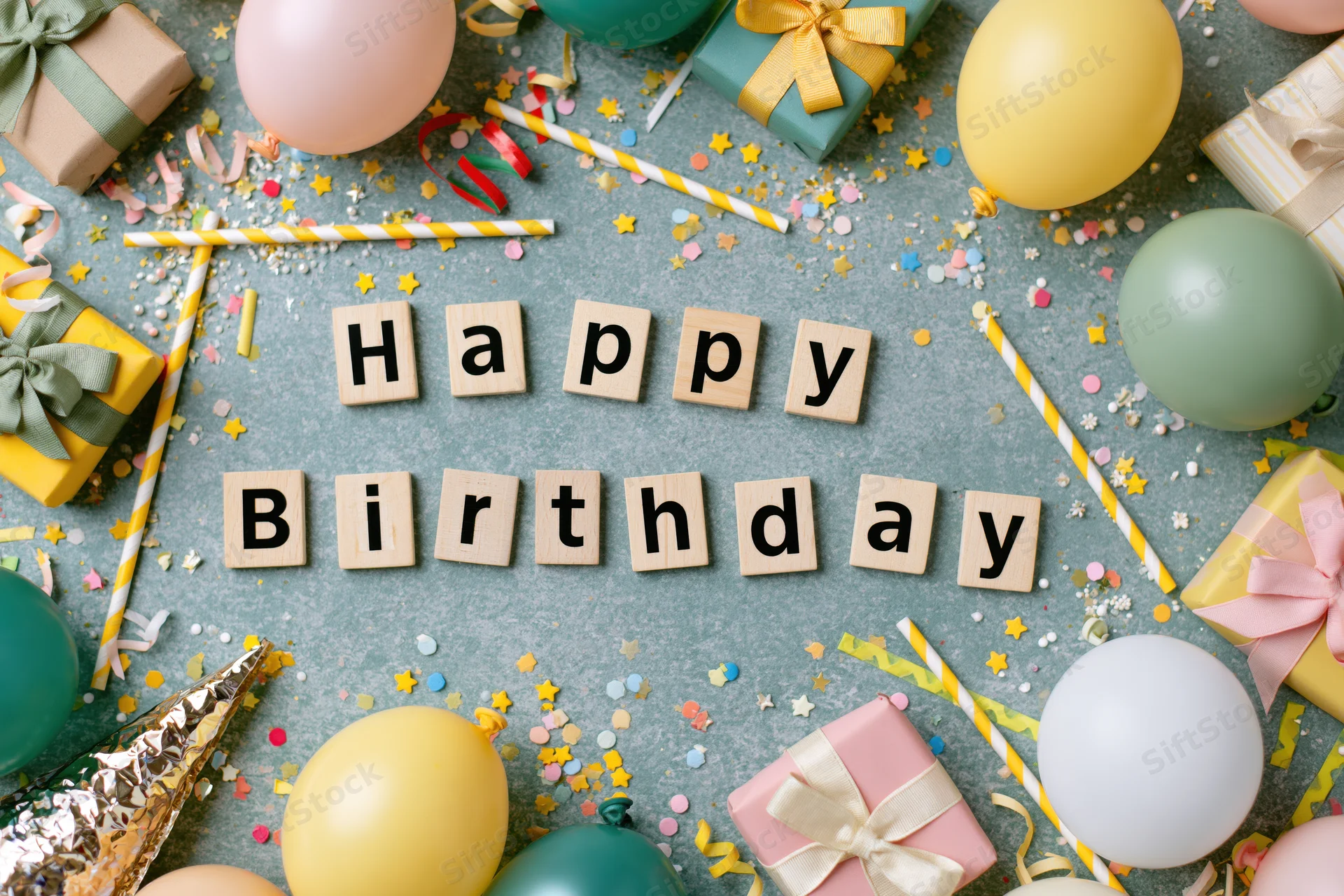 Wooden blocks spelling happy birthday surrounded by party decorations on a flat surface