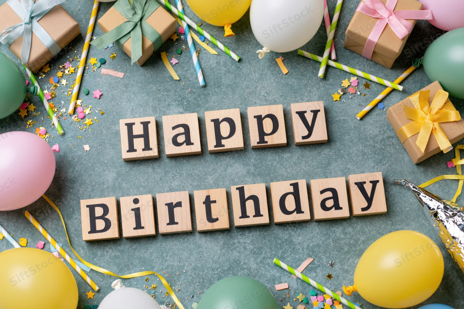 Wooden blocks spelling happy birthday surrounded by party decorations on a flat surface