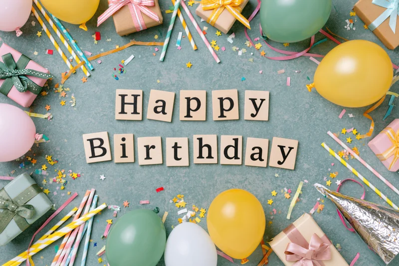 Wooden letter tiles spelling happy birthday surrounded by party supplies on gray surface