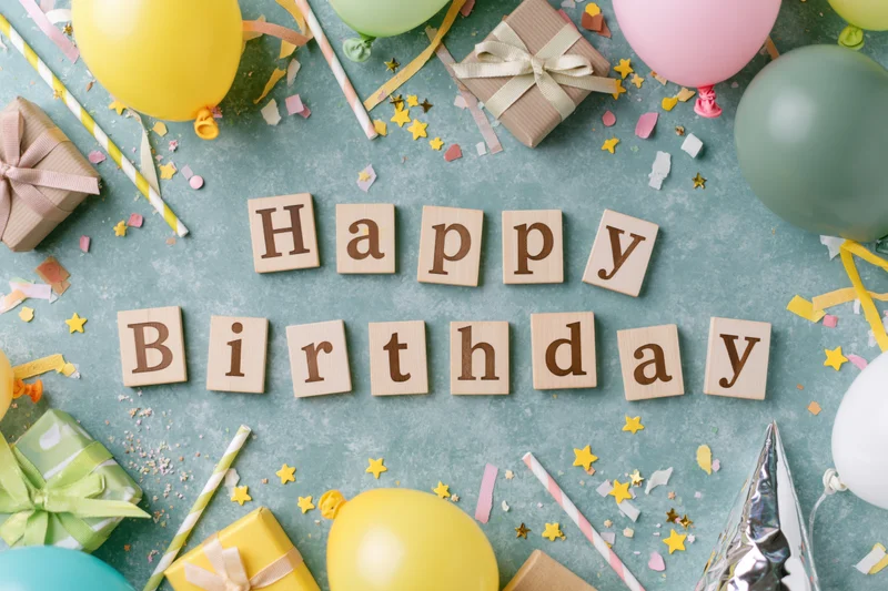 Wooden blocks spelling happy birthday surrounded by party supplies on a flat surface