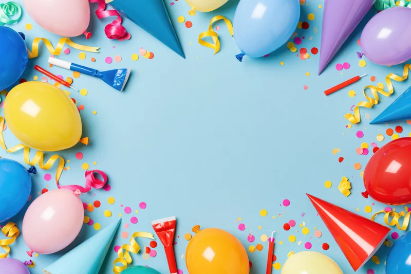 Colorful birthday party supplies arranged in a circular frame on blue background with copyspace in center
