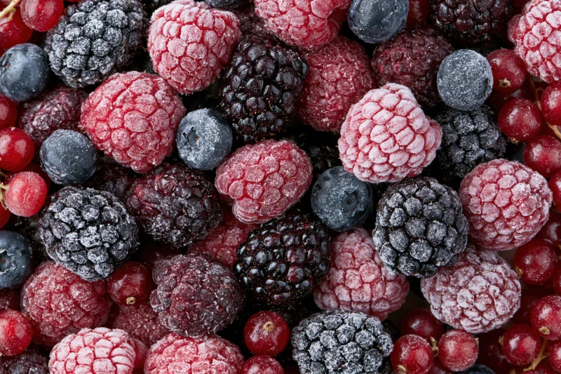 Closeup of mixed frozen berries including raspberries, blackberries and blueberries arranged in a flat lay