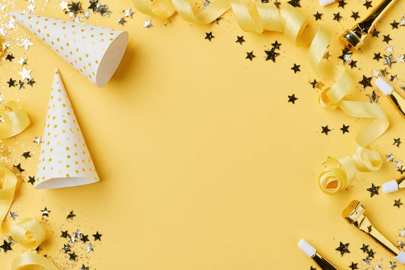 Party supplies arranged around edges of yellow surface with copyspace in center