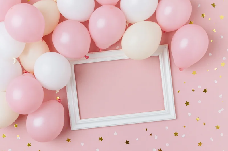 White frame surrounded by pink and white balloons on a pink surface with gold stars and confetti