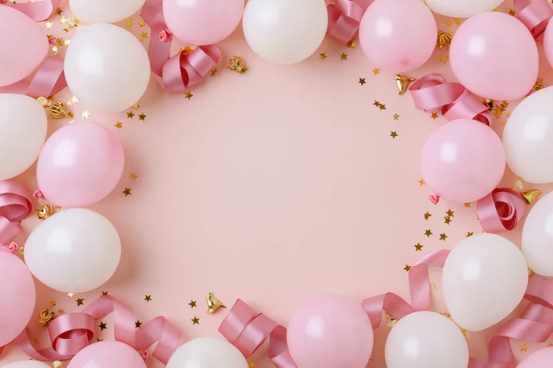 Pink and white balloons with curled ribbon and gold stars arranged in a frame on a pastel pink surface with copyspace in center