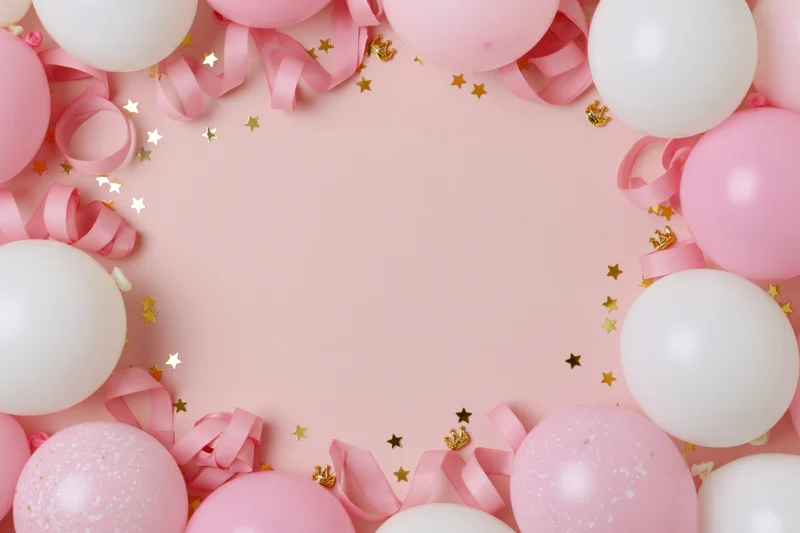 Pink and white balloons with curled ribbon and gold stars arranged in a frame on a pastel pink surface