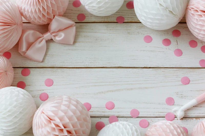 Pink and white honeycomb paper balls with satin bow arranged on wooden surface for party decoration