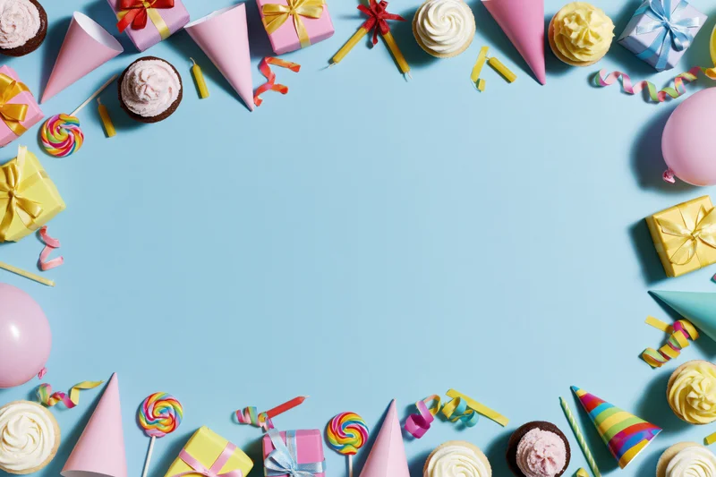 Colorful birthday party supplies arranged in a border around a light blue surface with copyspace in the center