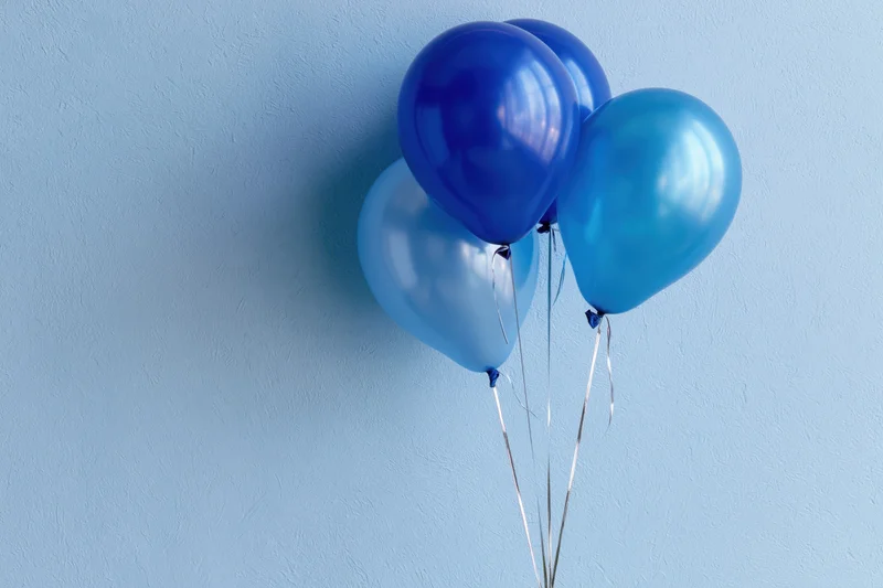 Four blue helium balloons clustered together against a light blue textured wall