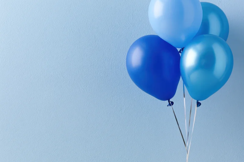 Four blue helium balloons clustered together against a light blue wall with copyspace on the left