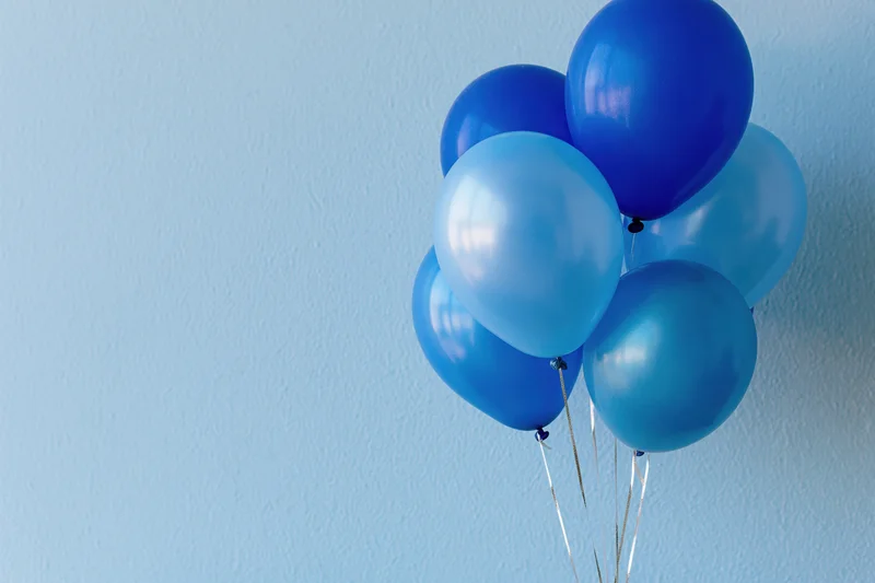 Cluster of blue helium balloons floating against a light blue textured wall with copyspace on the left