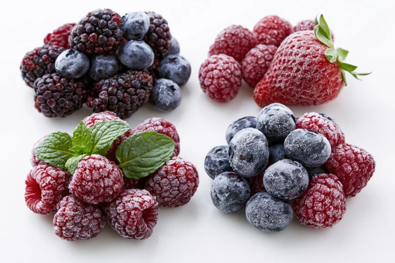 Four piles of frost-covered frozen berries with mint leaves on white background