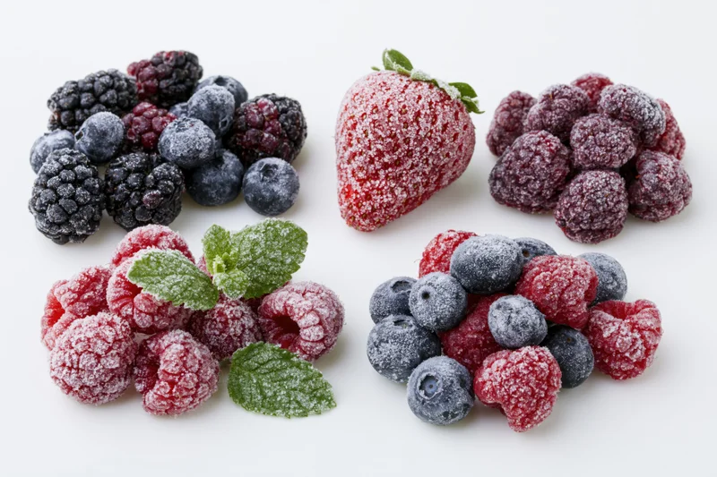Frost-covered berries arranged in small piles on white background with mint leaves