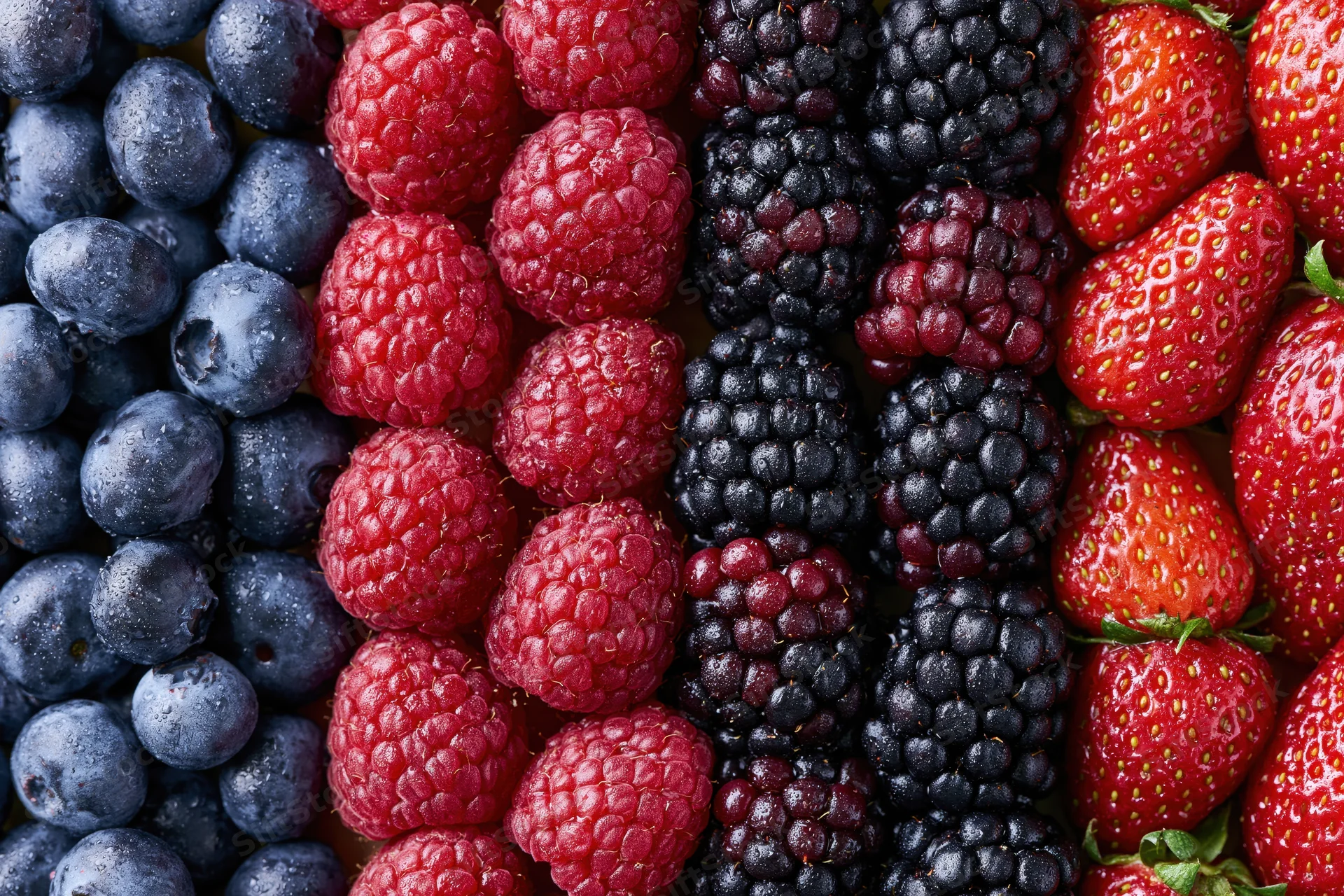 Four varieties of fresh berries arranged in vertical stripes