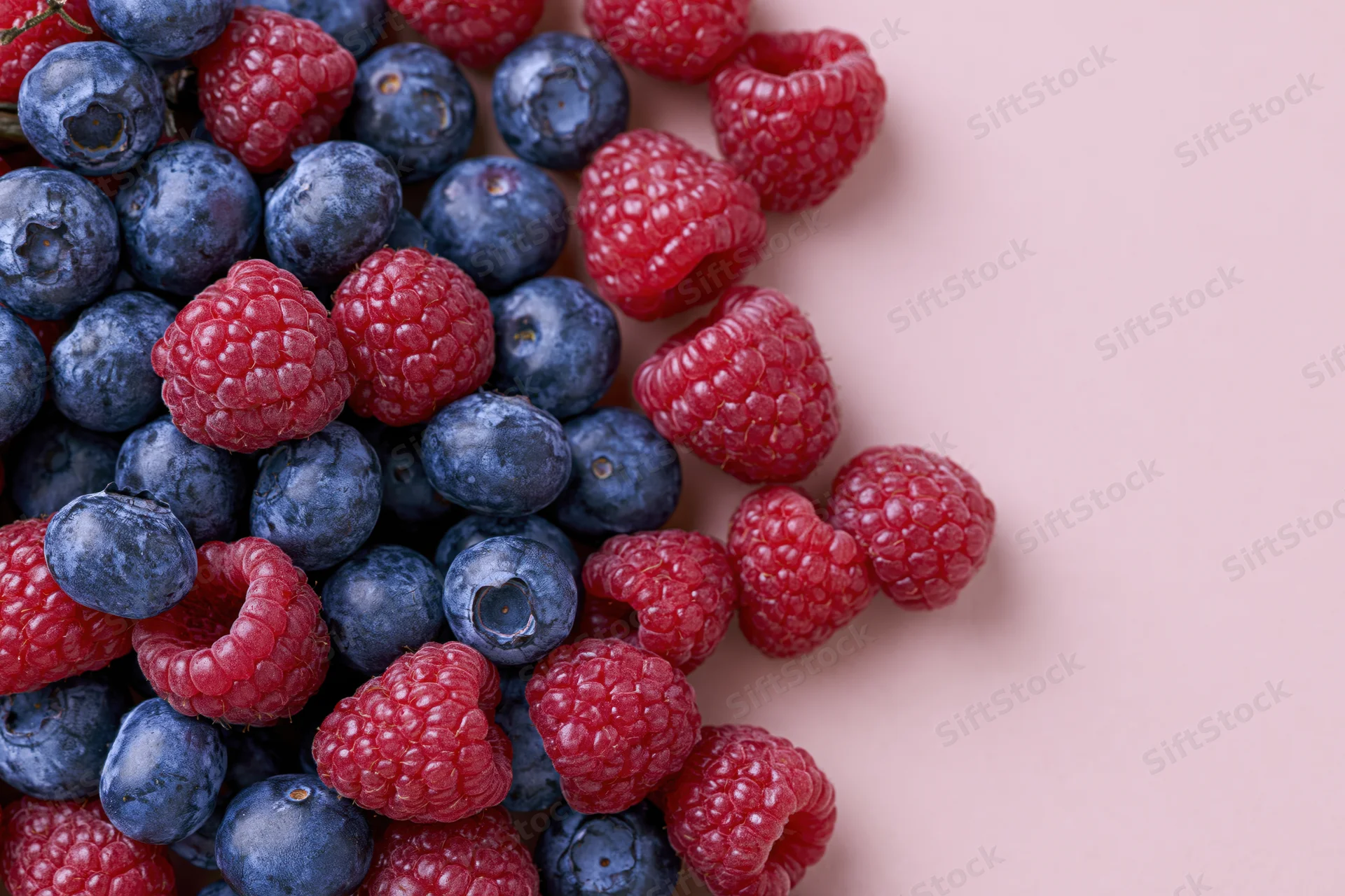 Blueberries and raspberries scattered on a pink surface with copyspace