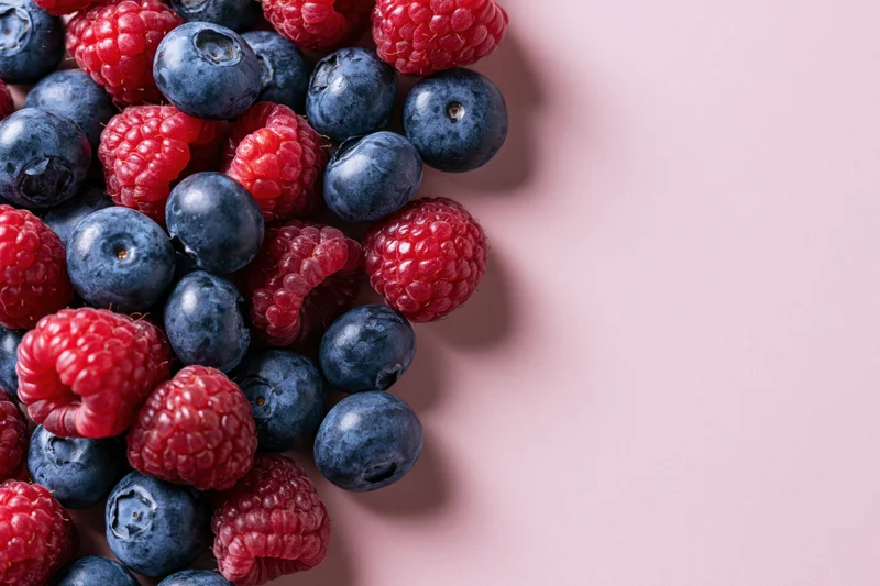 Blueberries and raspberries scattered on a pink surface with copyspace