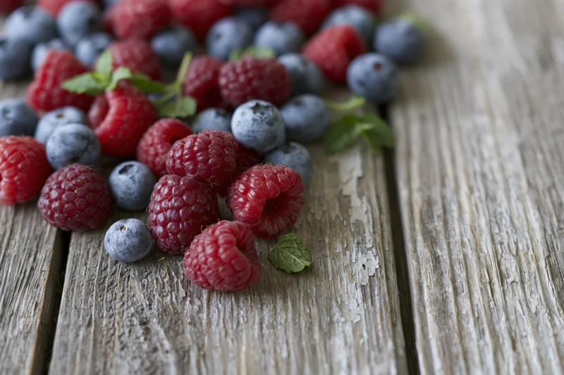 Fresh raspberries and blueberries scattered on a weathered wooden surface with mint leaves