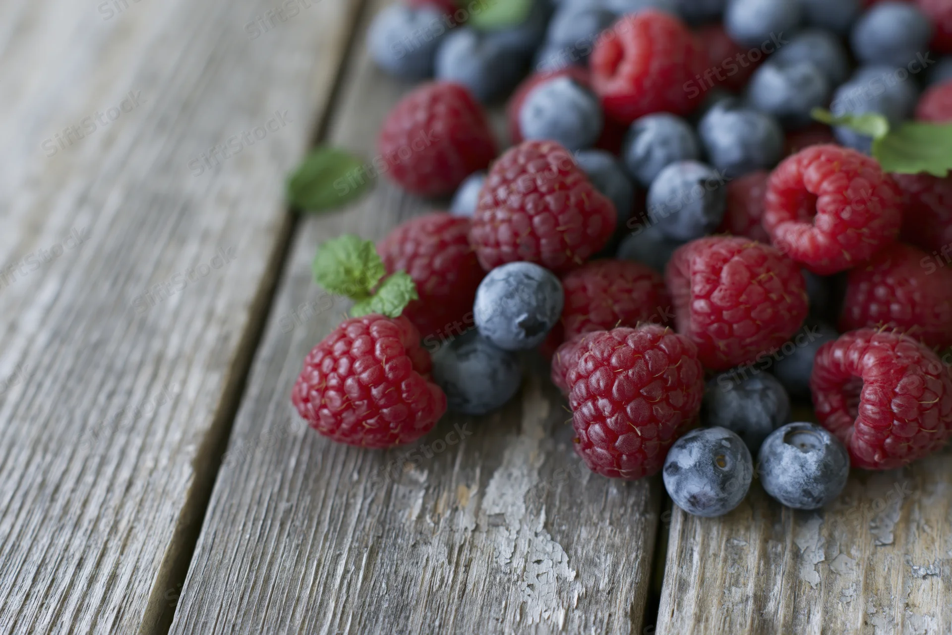 Fresh raspberries and blueberries scattered on a rustic wooden table